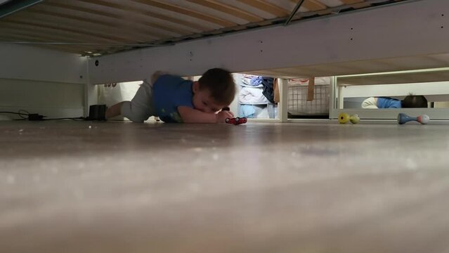 Happy toddler baby boy playing with toys under the bed. Kid aged one year three months (15 months)