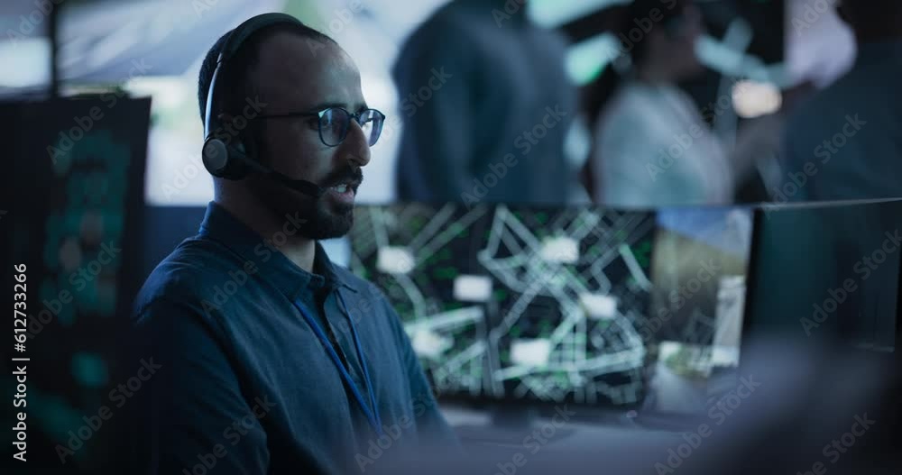 Poster Multiethnic Male Officer Works on a Computer with Surveillance CCTV Video Footage in a Traffic Monitoring Center with Multiple Feeds on a Big Digital Screen. Employee Having a Call with a Specialist