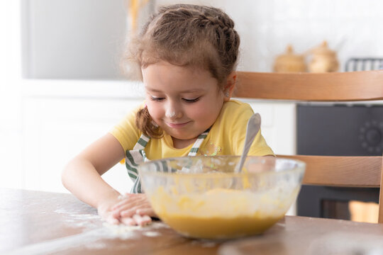 Happy child playing with flour in kitchen. kid cooking food. little cute girl in apron in preparing dough, baking pie, cookies, making biscuit