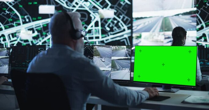 Technical Support Manager Using Headphones and a Computer with Green Screen Mock Up Display. Specialist in a Dark High-Tech Monitoring Room, Concentrated on a Call and Computer Work