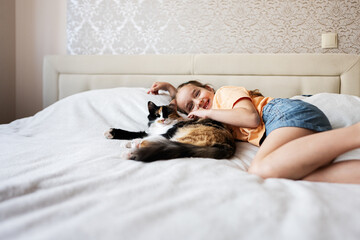 Cute little girl playing with her cat on the bed at home
