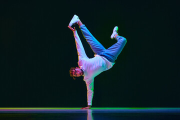 Dynamic image of talented, active young man in sport style clothes dancing breakdance against black studio background in neon light