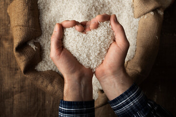 Human hands in shape of heart holding handful of rice over burlap sack