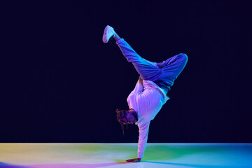 Youth culture. Young man in casual clothes making performance, dancing breakdance against black studio background in neon light