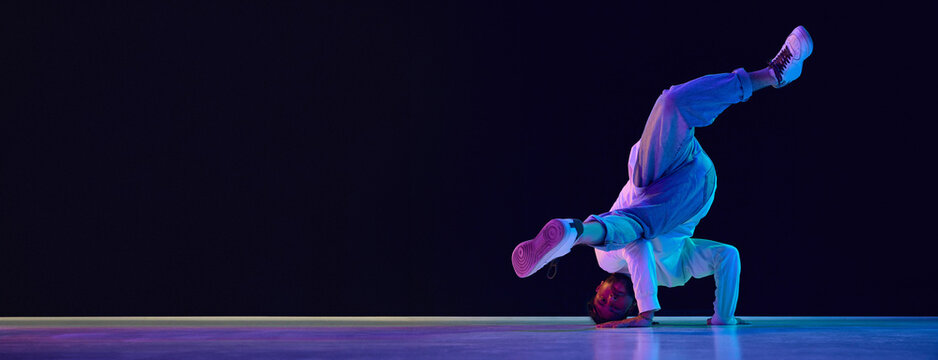 Young active man in casual clothes dancing hip-hop, breakdance against black studio background in neon light