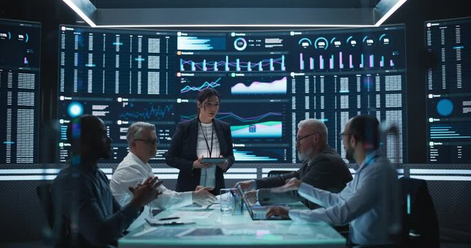 Diverse Team Of Data Scientists and Software Developers Discussing Reports in Monitoring Room with Analytics Feed on Big Digital Screen. Female Leading Artificial Intelligence Company Board Meeting