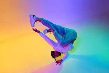 Fototapeta na wymiar Creative young guy in casual clothes dancing hip-hop contemporary, breakdance against gradient studio background in neon light