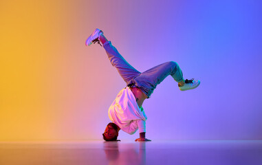 Creative young guy in casual clothes dancing hip-hop contemporary, breakdance against gradient studio background in neon light - obrazy, fototapety, plakaty