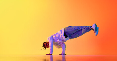 Standing on hands. Young guy making performance, dancing breakdance against gradient orange yellow studio background in neon light