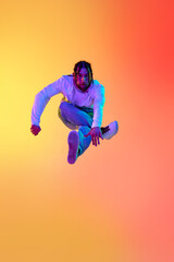 Fototapeta na wymiar Young bearded man with dreads in casual clothes dancing breakdance against gradient orange yellow studio background in neon light