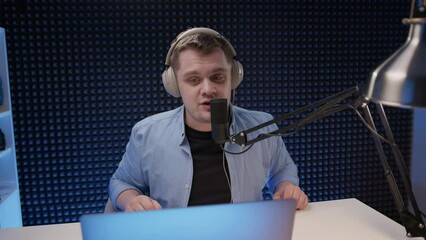 radio host sit in studio and communicates with audience. man in blue shirt and headphones sits in recording studio in front of professional microphone. announcer reads text for video. 