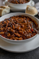 Stew with kidney beans, baked, beans, chicken meat and vegetable on a plate with spoon