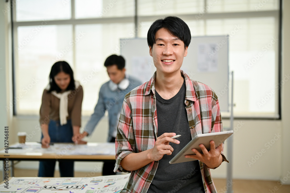 Canvas Prints a smart asian male website developer stands in the office with a digital tablet in his hand