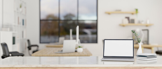A laptop white screen mockup on a white tabletop in modern minimal bright office.