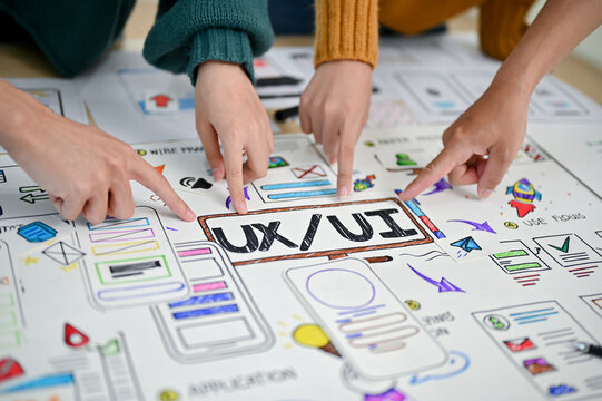 A close-up image of a developer's fingers pointing at UI and UX prototype paper on a table.