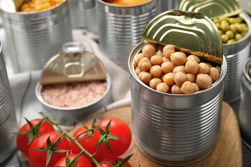 Open tin cans with chickpeas and different products on wooden table, closeup