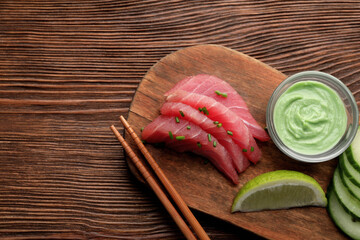 Tasty sashimi (pieces of fresh raw tuna) served with wasabi sauce and lime wedge on wooden table,...