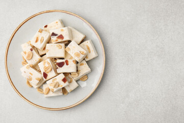 Pieces of delicious nutty nougat on light gray table, top view. Space for text