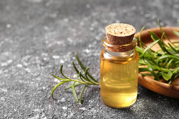 Bottle with essential oil and fresh rosemary on grey textured table, closeup. Space for text