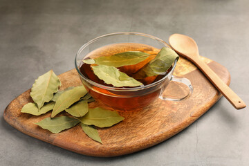 Cup of freshly brewed tea with bay leaves on grey table