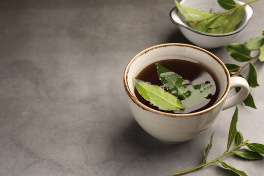 Cup of freshly brewed tea with bay leaves on grey table, space for text