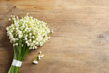 Beautiful lily of the valley bouquet on wooden table, top view. Space for text