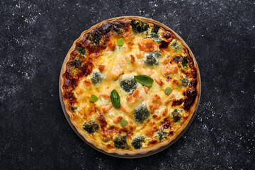 Delicious homemade quiche with salmon and broccoli on black table, top view