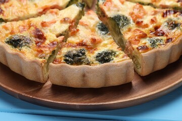 Delicious homemade quiche with salmon and broccoli on wooden board, closeup