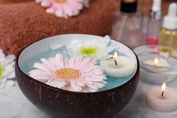 Beautiful composition with bowl of water, flowers and candles on light table, closeup. Spa treatment