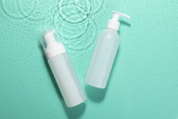 Bottles of face cleansing product on water against turquoise background, flat lay