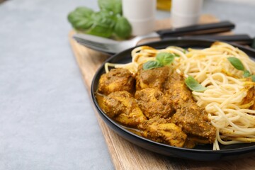 Delicious pasta and chicken with curry sauce served on grey table, closeup. Space for text