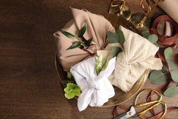 Furoshiki technique. Flat lay composition with gifts packed in different fabrics and flowers on wooden table