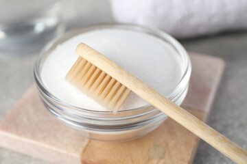 Bamboo toothbrush and glass bowl of baking soda on light table, closeup