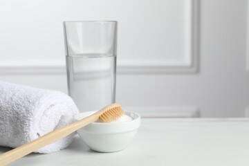 Fototapeta na wymiar Bamboo toothbrush, bowl of baking soda, towel and glass of water on white table. Space for text