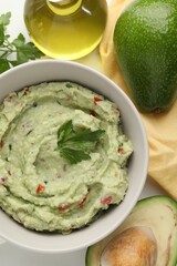 Delicious guacamole and ingredients on white table, flat lay