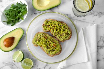 Delicious sandwiches with guacamole and ingredients on white marble table, flat lay