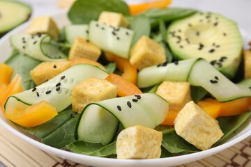 Bowl of tasty salad with tofu and vegetables on bamboo mat, closeup