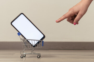 Ecommerce concept image: woman pointing a cart with a blank screen smartphone inside