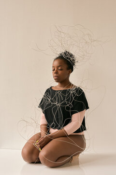 Young African American woman sitting on her knees with eyes closed entangled in white wire