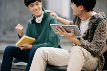 Two smart young Asian college students focusing on his school project, looking at laptop and tablet, discussing and working together at the campus park .