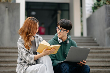 Two smart young Asian college students focusing on his school project, looking at laptop and tablet, discussing and working together at the campus park .