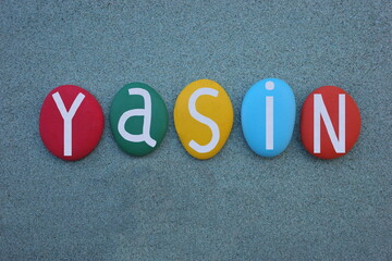 Yasin, turkish masculine given name composed with multi colored stone letters over green sand