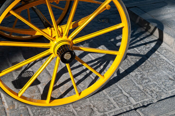 Vista de la rueda amarilla de un carro de caballos para pasear turistas en una calle de una ciudad andaluza. - obrazy, fototapety, plakaty