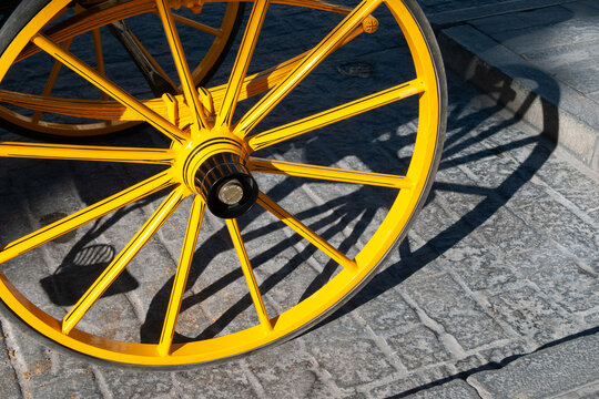 Vista de la rueda amarilla de un carro de caballos para pasear turistas en una calle de una ciudad andaluza.
