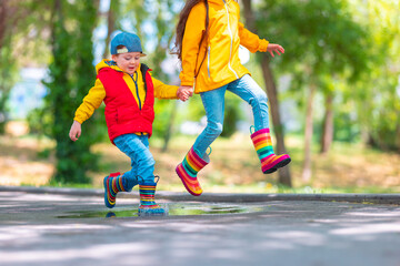 Happy kids girl and boy with umbrella and colorful rubber rain boots playing outdoor and jumping in rainy puddle