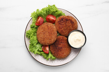 Plate with delicious vegan cutlets, lettuce, tomatoes and sauce on white marble table, top view