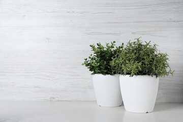 Different artificial potted herbs on white wooden table, space for text