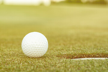 A golfer puts a golf ball on a green golf, the glare in the sun sets in the evening.