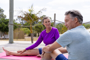 Caucasian senior woman looking at husband while practicing yoga on hardwood floor at tourist resort