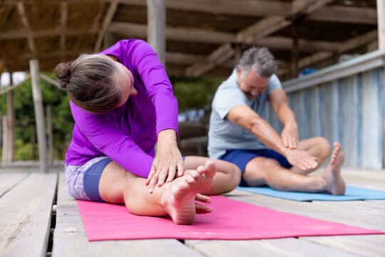Caucasian senior couple stretching hands and legs while practicing yoga on floor at tourist resort